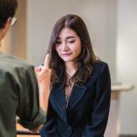 Reaw view of Furious boss scolding asian young businesswoman in formal suit by point to her face in modern office, Business mistake and punish concept
