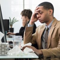 Business man working at his desk sick with a cold and fever Business man working at his desk sick with a cold and fever